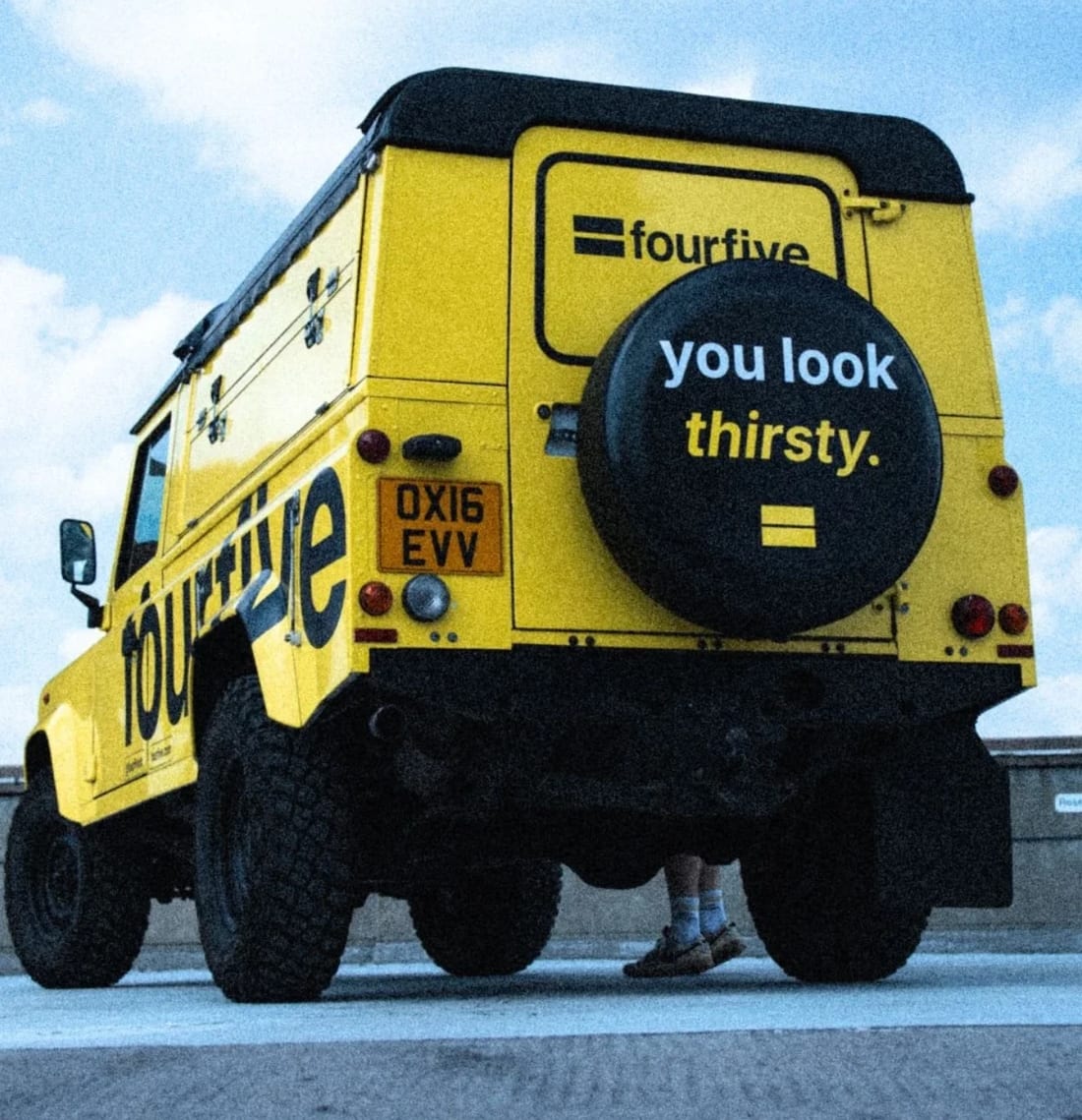 fourfive's yellow Land Rover Defender from behind, its spare wheel cover reading “you look thirsty.”