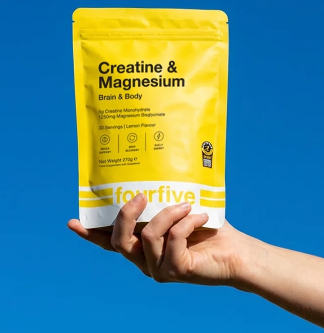 A hand holding a fourfive Creatine & Magnesium pouch up against a clear blue sky