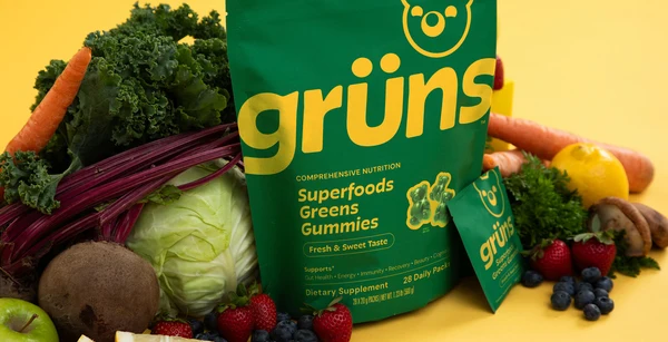 A Grüns pouch on yellow, surrounded by kale, carrots, beetroot, cabbage, berries and other whole produce